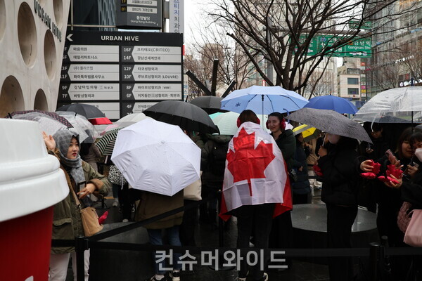 팀홀튼 국내 1호 매장 앞 소비자들이 비가 오는 가운데 우산을 쓰고 오픈을 기다리고 있다. 이;중 캐나다 국국기를 어깨에 덥고 있는 외국인이 시선을 사로잡았다./ 사진: 전휴성 기자
